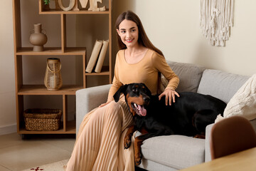 Cute Doberman dog and beautiful young happy woman sitting on sofa at home