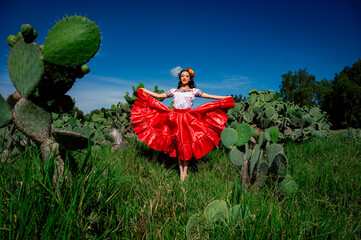 Mexican folkloric dancer in traditional red dress among cactus field