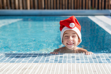 A child wearing a Santa Claus hat in an outdoor pool with blue water. New Year and Christmas. Christmas holidays. Tourism. New Year's Eve in warm countries
