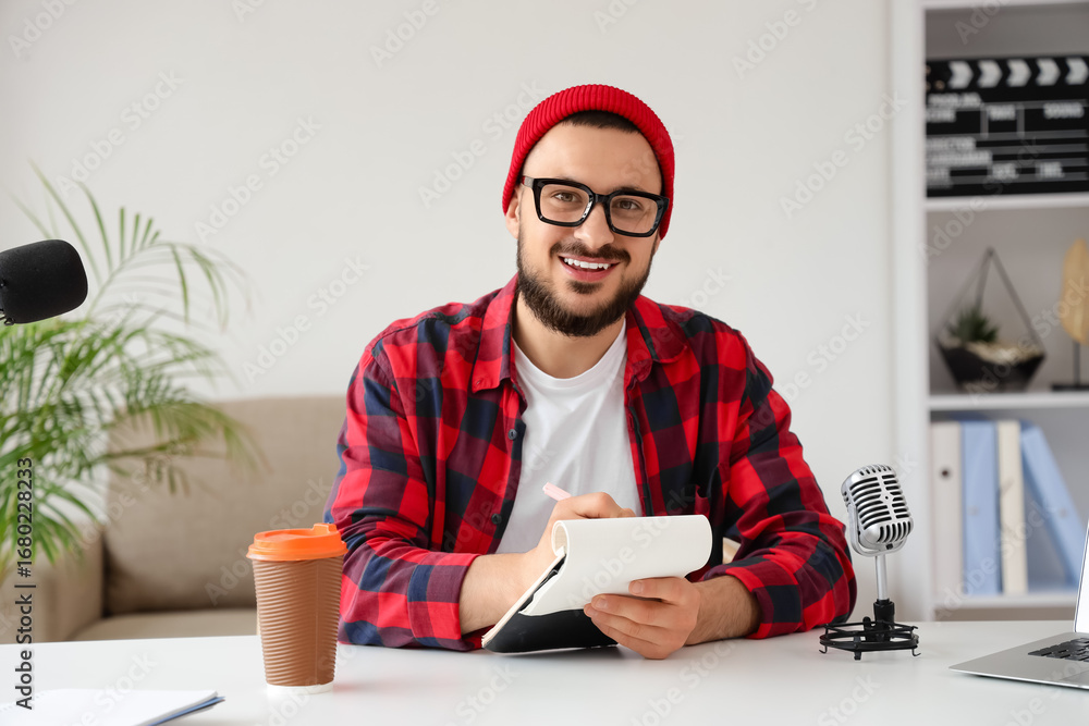 Poster handsome man with notebook recording podcast at table in studio