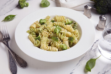 Plate of delicious fusilli pasta with broccoli and basil leaves on white background, closeup