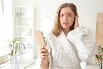 Worried young woman with hair loss problem and brush in bathroom