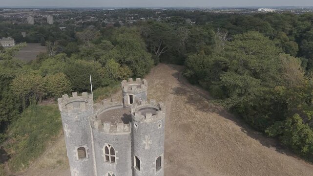Aerial drone footage at Blaise Castle, Henbury, Bristol. It begins close above the three turrets, reversing and rising to show the castle grounds, surrounding woodland, and distant urban landscape.