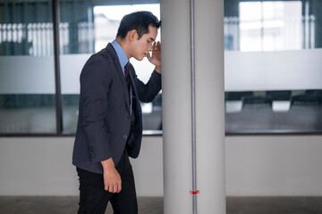 Stressed businessman leaning against pillar in office hallway
