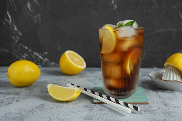 Glass of Long Island iced tea cocktail with mint and lemons on grey table
