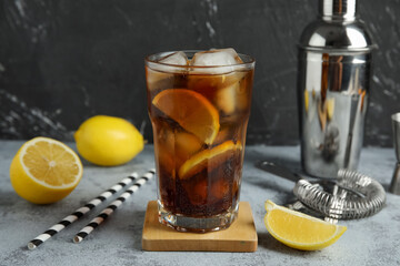 Glass of Long Island iced tea cocktail and lemons on grey table