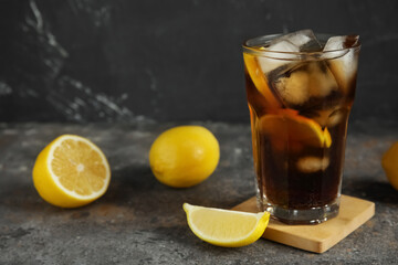 Glass of Long Island iced tea cocktail and lemons on dark table