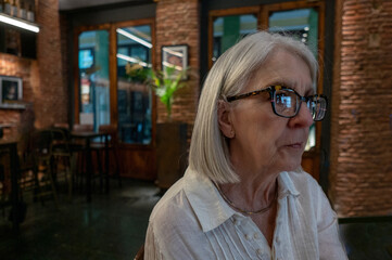 Senior Woman Sitting in a Cozy Cafe Wearing Glasses and Reflecting