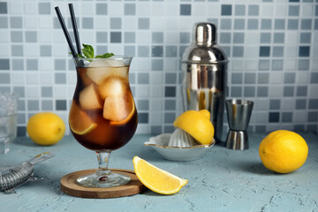 Glass of Long Island iced tea cocktail with mint and lemons on light blue table