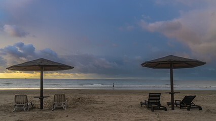 Sun beds and umbrellas on the sandy beach. Evening. The clouds in the blue sky are highlighted in...
