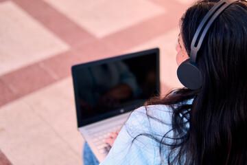 Back view of an adult professional woman working online and typing on her laptop, wearing...