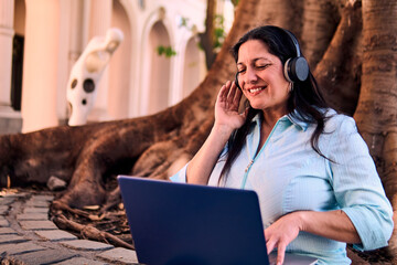 Beautiful adult Latina professional working online, wearing headphones and listening to music...