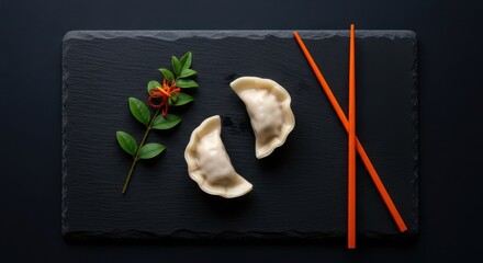 Fototapeta premium A topdown view of two delicious dumplings served with chopsticks on a dark slate plate with a sprig of greenery