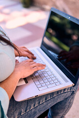 View of the hands of an adult professional woman typing on a laptop, working online, connecting to the internet, and studying. She's using her cell phone, at home, outdoors. Planning, home office.