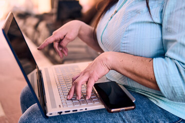 View of the hands of an adult professional woman typing on a laptop, working online, connecting to...