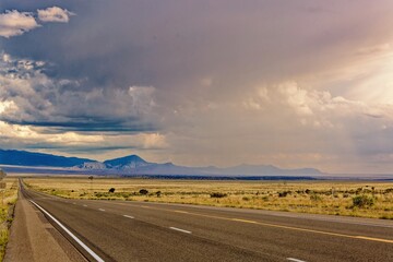 Fototapeta premium Open road highway leading to distant mountains under dramatic storm clouds