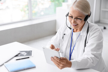 Female doctor with headset and tablet computer giving online consultation in clinic