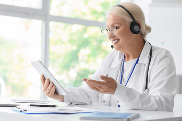 Female doctor with headset and tablet computer giving online consultation in clinic