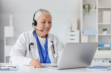 Female doctor in headset with laptop giving online consultation at hospital