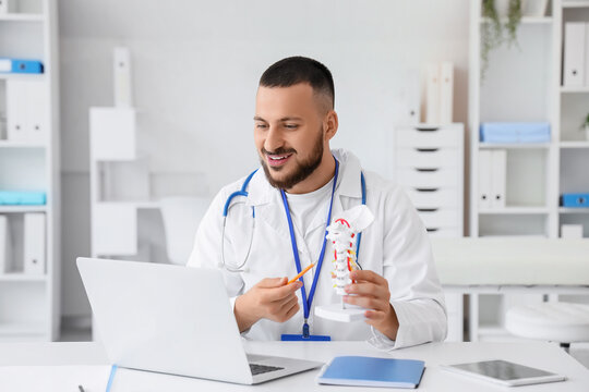 Male doctor with spine model and laptop giving online consultation in clinic