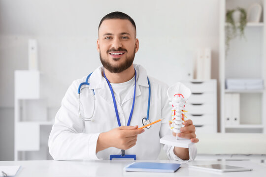 Male doctor with spine model giving online consultation in clinic - Powered by Adobe