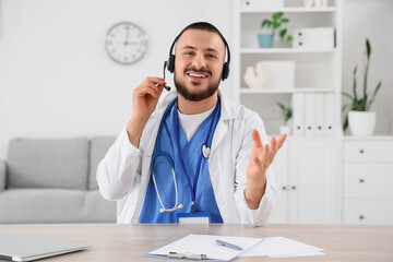 Male doctor with headset giving online consultation at table in clinic
