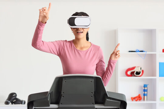 Young African-American woman in VR glasses using virtual screen on treadmill at gym