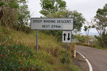 Steep Winding Descent road sign in a rural area with grass and trees