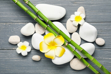 Beautiful spa composition with stones, plumeria flowers and green twigs on grey wooden background,...