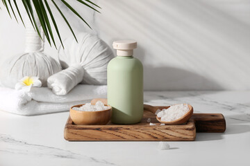Spa composition with wooden board, bottle of cosmetic product, bowl and scoop with sea salt on marble background, closeup