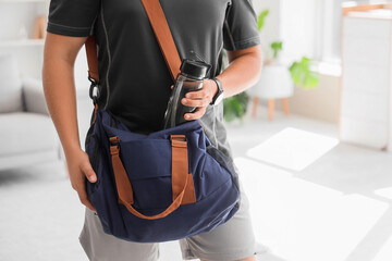 Young man putting bottle of water into sports bag at home