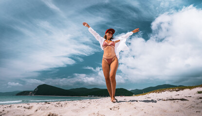 Stylish woman dancing barefoot on beach, arms open to sky in joyful motion. Her body expression shows lightness, energy, and pure connection with nature in summer moment.