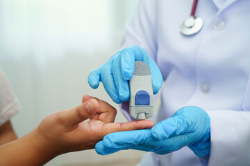 Asian woman self testing to check blood sugar level diabetes by digital lancet on finger at home.