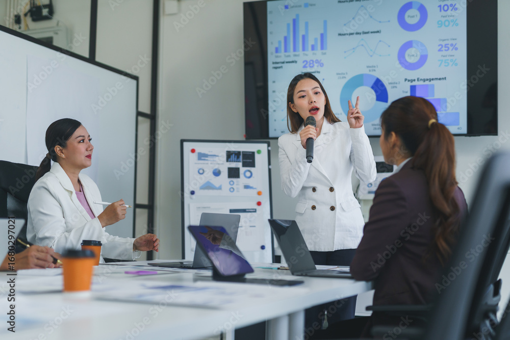 Poster businesswoman using a microphone during a presentation with charts and graphs in a meeting room with