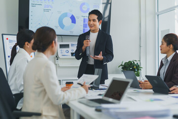 Businessman using microphone and gesturing while giving presentation to colleagues in modern office