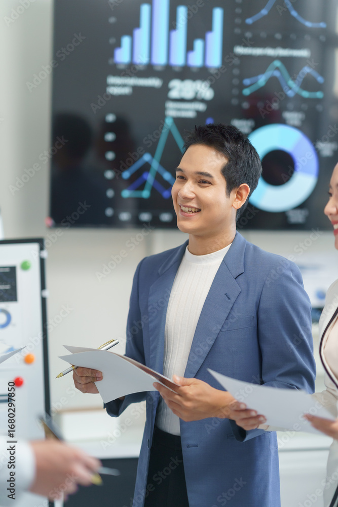 Poster young manager holding documents and smiling while discussing financial charts with colleagues in a m