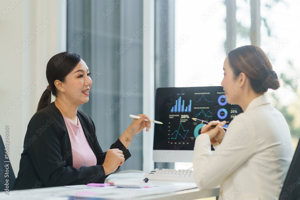 Poster two businesswomen analyzing marketing data on computer screen, discussing strategy and pointing at c