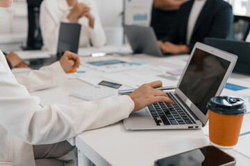 Businesswoman collaborating with colleagues while using a laptop during a meeting, actively working together on a project in a modern office setting