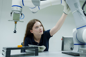 young female trainee adjusts robotic arm position during hands on robotics training class...