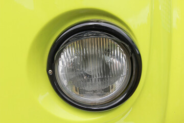 A detailed close-up shot of the round headlight of a classic yellow vintage car.