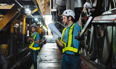Two men in safety gear are looking at  piece of machinery