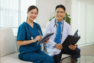 Two doctors are sitting on  couch, one of them holding tablet