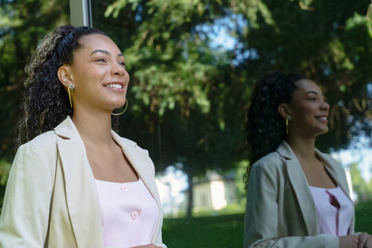 Young manager smiling, enjoying career success, reflecting in window glass with trees in background