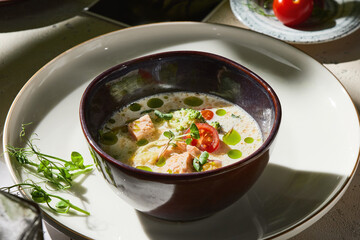 Salmon creamy fish soup in bright rustic lighting, overhead composition with fresh herbs and vegetables