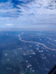 Airplane glides above winding river, revealing aerial landscape with clouds, farmland, settlements, and blue sky, creating perspective of travel, journey, freedom, and scenic natural beauty.