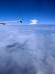 Airplane wing view above the clouds, showing bright blue sky, fluffy white formations, and stunning aerial scenery that captures the beauty of flight and peaceful travel moments.