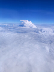 Fototapeta premium Expansive view above the clouds with a bright blue sky and towering cumulus formation, showcasing the beauty of aerial landscapes, peaceful atmosphere, and high-altitude travel scenery.