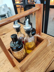 Wooden condiment box storage holds seasoning bottles with chili powder, garlic oil, pepper mix, spice blend, rustic kitchen decor, restaurant table detail, and culinary dining accessory design.