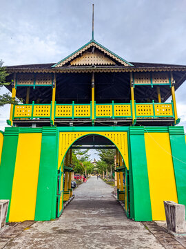 Colorful green and yellow gate of Kadariyah Palace welcomes visitors with traditional Malay architecture, an ornate balcony, and a paved pathway through the entrance in Pontianak.