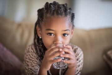 Black Kid Girl Drinking Water: Hydrating at Home on Sofa. African American Teenager with Glasses